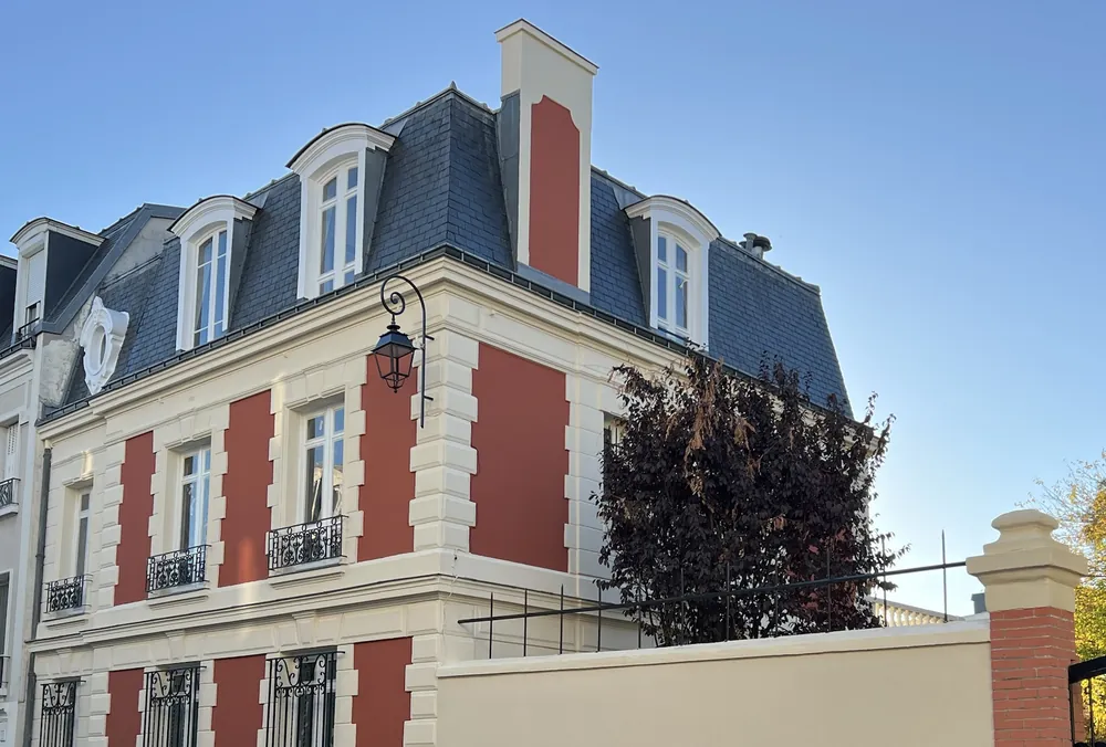 Maison bourgeoise à toit mansardé en ardoise, panneaux rouge terre cuite et encadrements crème.