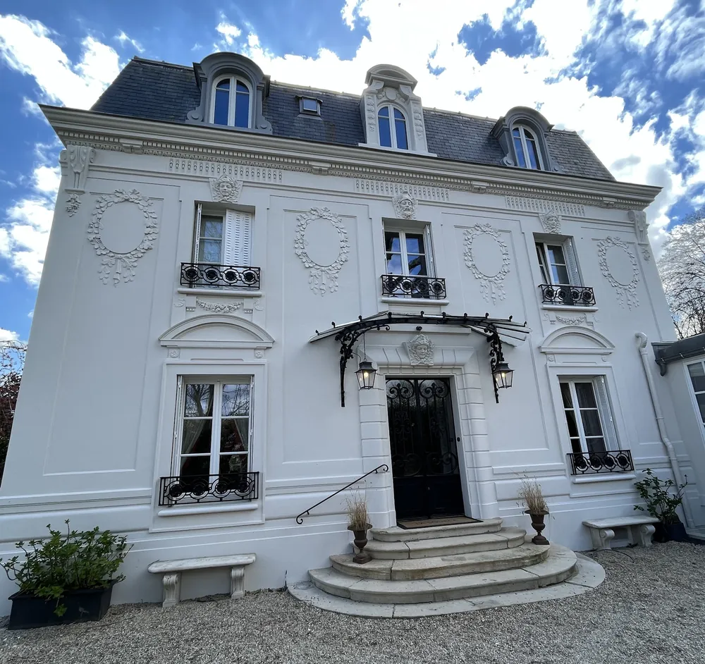 Maison de maître blanche ornée de médaillons sculptés, marquise en fer forgé au-dessus de la porte et perron arrondi.